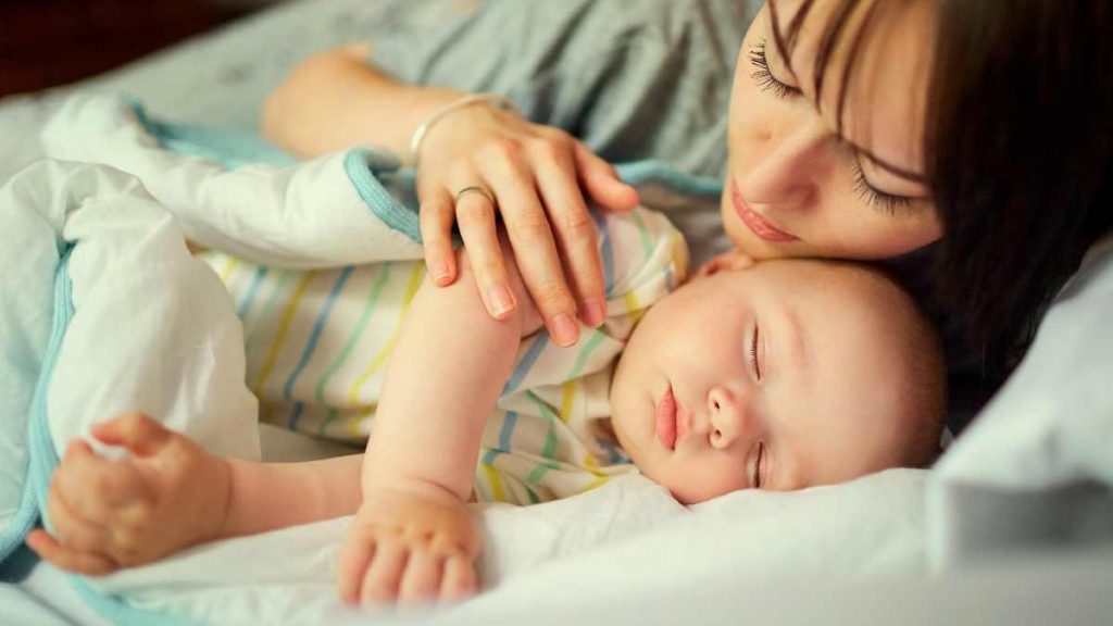 baby sleeping next to mom in bed