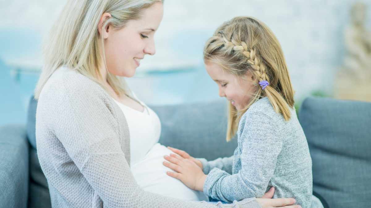 girl holding her moms pregnant bump looking forward to meeting baby