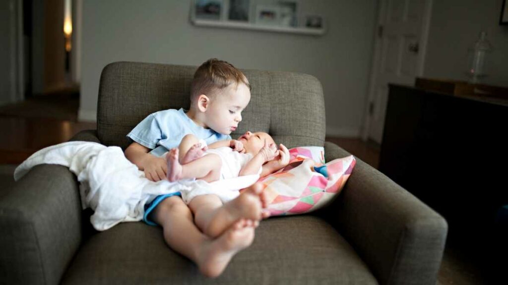 sibling helping with newborn on couch